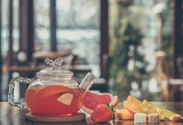 Fruit red tea in a glass kettle and cup on the wooden background