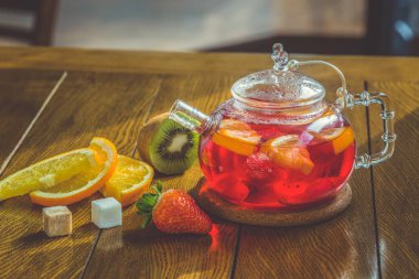 Cam çaydanlıkta meyveli kırmızı çay ve ahşap arka planda fincan.