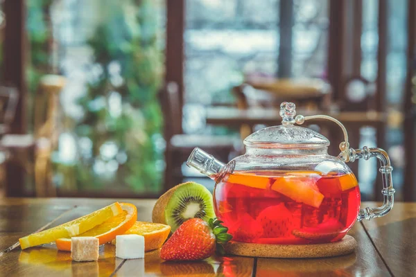 Fruit red tea in a glass kettle and cup on the wooden background