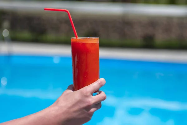 juice in a glass on the wooden table by the pool.