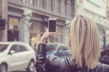 Kadın turist sokakta cep kamerasıyla fotoğraf çekiyor.