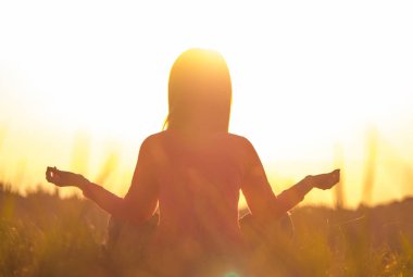 Gün batımında yoga yapan bir kadının arka ışığı.