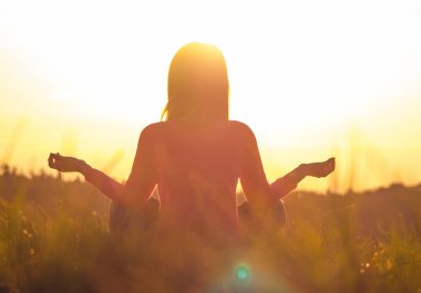 Gün batımında yoga yapan bir kadının arka ışığı.