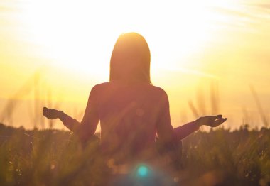 Gün batımında yoga yapan bir kadının arka ışığı.