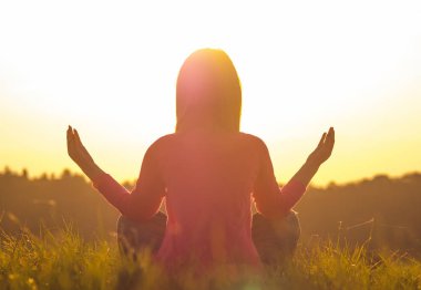 Gün batımında yoga yapan bir kadının arka ışığı.