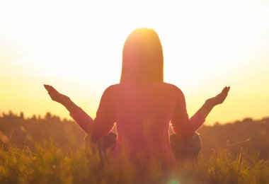 Gün batımında yoga yapan bir kadının arka ışığı.