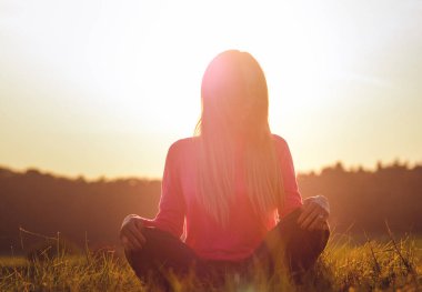 Genç kadın gündoğumu arka plan üzerinde yoga yapıyor. Sanatsal tonlama.