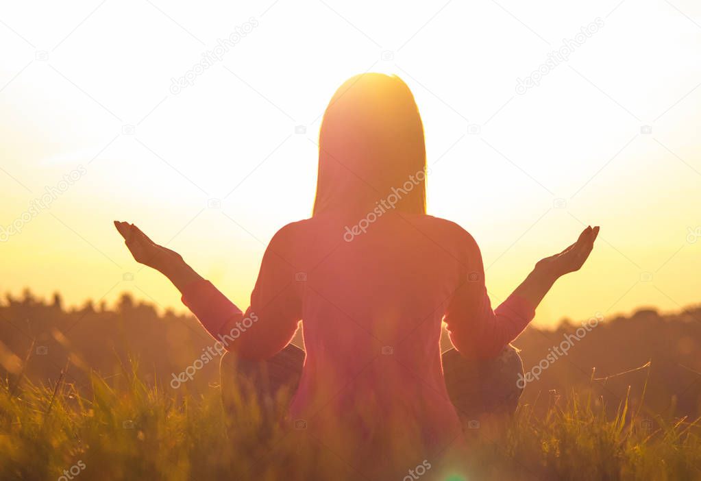 Back light of a woman exercising yoga at sunset with a warmth background