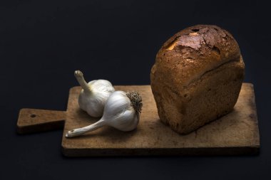 Karanlık ekmek ve siyah bir zemin üzerine sarımsak.