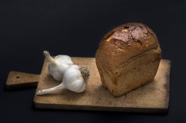 Karanlık ekmek ve siyah bir zemin üzerine sarımsak.