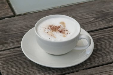 Ahşap bir masa üzerinde beyaz bir fincan cappuccino kahve