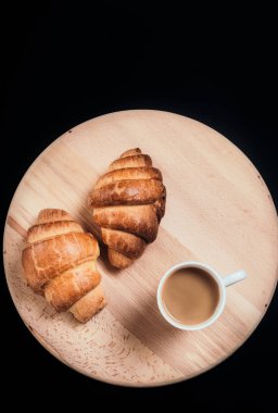 İki taze kruvasanlar ve kupa kahve ile görünümünü yukarıda peçete tablo siyah arka plan üzerine yerleştirilen