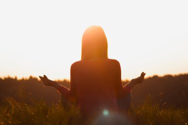 Gün batımında yoga yapan bir kadının arka ışığı.