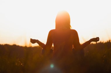 Gün batımında yoga yapan bir kadının arka ışığı.