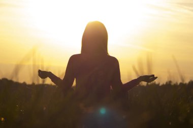 Gün batımında yoga yapan bir kadının arka ışığı.
