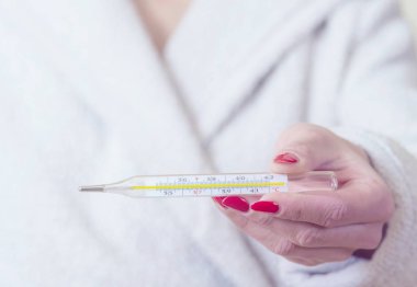 Ellerinde termometre tutan kadın gripten acı çekerken vücut ısısını ölçüyor..