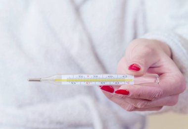 Ellerinde termometre tutan kadın gripten acı çekerken vücut ısısını ölçüyor..