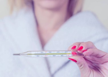 Ellerinde termometre tutan kadın gripten acı çekerken vücut ısısını ölçüyor..