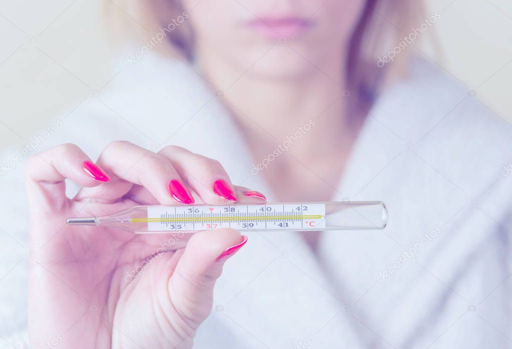 woman holding thermometer in hands, measuring body temperature while suffering from influenza.