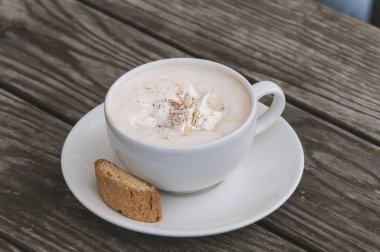 Ahşap bir masa üzerinde beyaz bir fincan cappuccino kahve