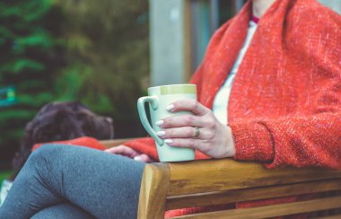 Bir kadın rahat bir ortamda sıcak içecek bir fincan tutar. Yakın bir köpek oturuyor