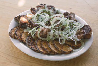 domuz şiş kebap ve ahşap bir masa üzerinde beyaz bir tabak patates