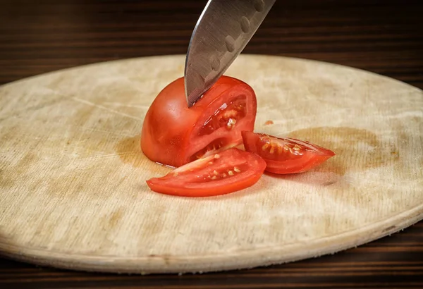 Koch schneidet eine Tomate auf einem Holztisch — Stockfoto