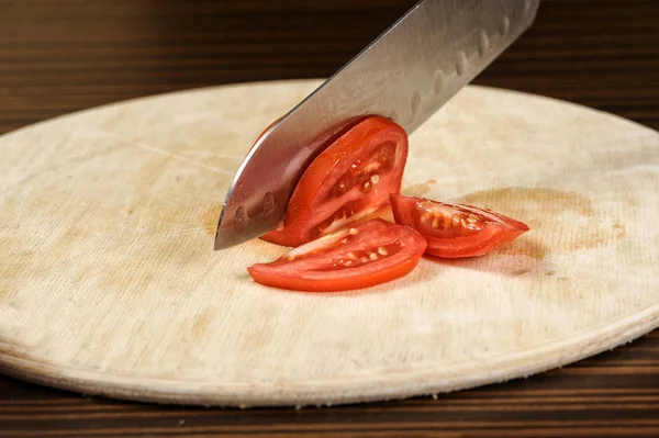Koch schneidet eine Tomate auf einem Holztisch — Stockfoto