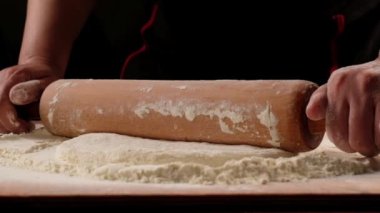 chef is rolling the dough with the rolling pin on the on the table. Hands close-up.Slow motion.Baker kneading dough for pizza  preparation. Chef cook making dough for baking pie on wooden table. Process preparation homemade pastry.food concept