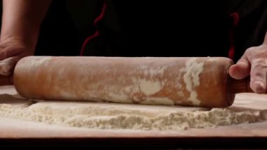 chef is rolling the dough with the rolling pin on the on the table. Hands close-up.Slow motion.Baker kneading dough for pizza  preparation. Chef cook making dough for baking pie on wooden table. Process preparation homemade pastry.
