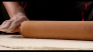 chef is rolling the dough with the rolling pin on the on the table. Hands close-up.Baker kneading dough for pizza  preparation. Chef cook making dough for baking pie on wooden table. Process preparation homemade pastry. 
