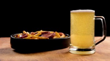 cold light beer with bubbles in a glass and fried sausages with potatoes on a wooden background