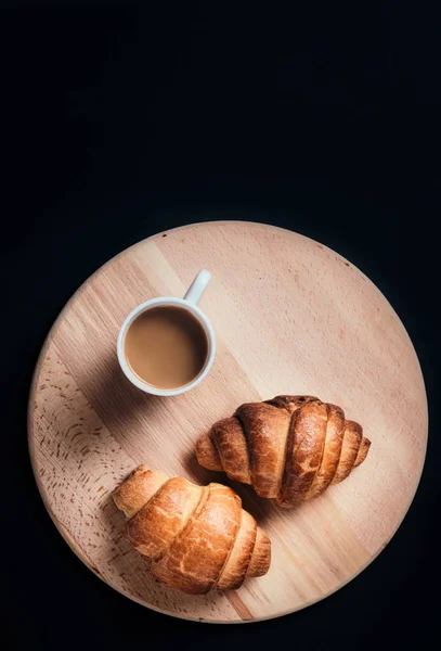Croissants recém-assados em tábua de madeira com xícara de café em b — Fotografia de Stock