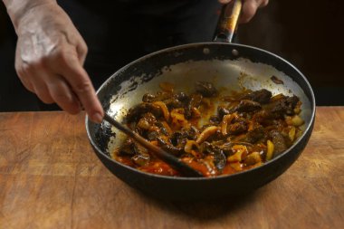 Şef tavada Çin yemeği pişiriyor, tahta kaşıkla karıştırıyor.