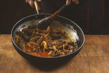 Şef tavada Çin yemeği pişiriyor, tahta kaşıkla karıştırıyor.