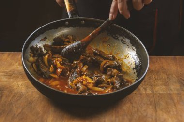 Şef tavada Çin yemeği pişiriyor, tahta kaşıkla karıştırıyor.