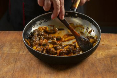 Şef tavada Çin yemeği pişiriyor, tahta kaşıkla karıştırıyor.