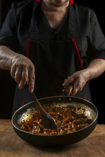 Chef cooks Chinese food in a pan, stirring with a wooden spoon