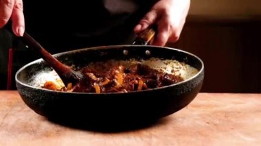 Şef bir tavada Çin yemekleri pişirir, tahta bir kaşıkla karıştırarak. Yavaş çekim