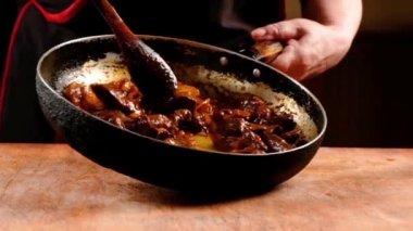 Şef bir tavada Çin yemekleri pişirir, tahta bir kaşıkla karıştırarak. Yavaş çekim