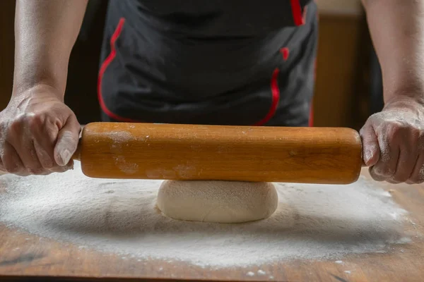 Baker kneading dough for pizza  preparation. Chef cook making dough for baking pie on wooden table. Process preparation homemade pastry. Cooking pasta, spaghetti,khachapuri, food concept