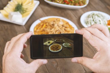 Yemek blogcusu akıllı telefon kullanarak fotoğraf çekiyor. Mans elleri geleneksel doğu yemeklerini telefonla çekiyor. Öğle ya da akşam yemeği. Sığır stroganoff. Sosyal medya ve blog için. Üst görünüm cep telefonu.