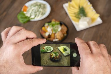 Gıda blogger fotoğraf çekmek akıllı telefon kullanarak . Mans eller geleneksel yemekler telefon fotoğrafçılığı yapmak. öğle yemeği ya da akşam yemeği et ve patates. Sosyal medya için, bloglama. En iyi görüntü cep telefonu.