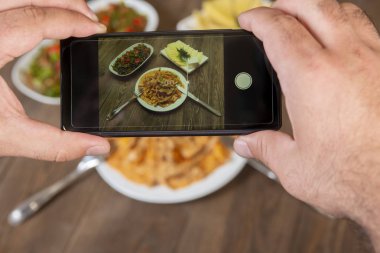 Yemek blogcusu akıllı telefon kullanarak fotoğraf çekiyor. Mans elleri geleneksel yemeklerin fotoğrafını çekiyor. Öğle ya da akşam yemeği. Sığır stroganoff. Sosyal medya ve blog için. Üst görünüm cep telefonu.