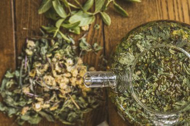 ahşap bir masada bir çaydanlık otlar ile çay.