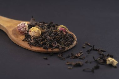 siyah arka plan üzerinde izole ahşap bir kaşık üzerinde gül çiçekleri ile aromatik siyah kuru çay
