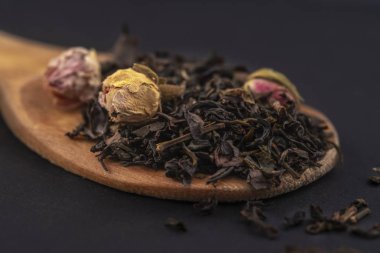 siyah arka plan üzerinde izole ahşap bir kaşık üzerinde gül çiçekleri ile aromatik siyah kuru çay