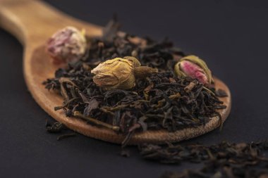 siyah arka plan üzerinde izole ahşap bir kaşık üzerinde gül çiçekleri ile aromatik siyah kuru çay