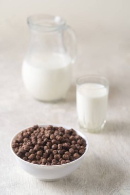 Beyaz ahşap arka planda çikolatalı mısır topu ve süt dolu bir kase..