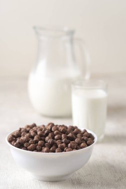 Beyaz ahşap arka planda çikolatalı mısır topu ve süt dolu bir kase..